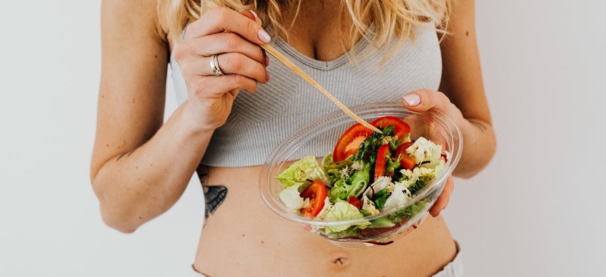 Woman in sports attire enjoys a fresh, nutritious salad, embodying a healthy lifestyle.
