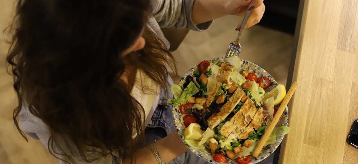 Overhead view of a woman eating a chicken salad balancing health with deliciousness.