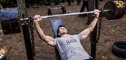 Man weightlifting outdoors, using a bench press setup amid trees for strength training.