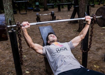 Man weightlifting outdoors, using a bench press setup amid trees for strength training.